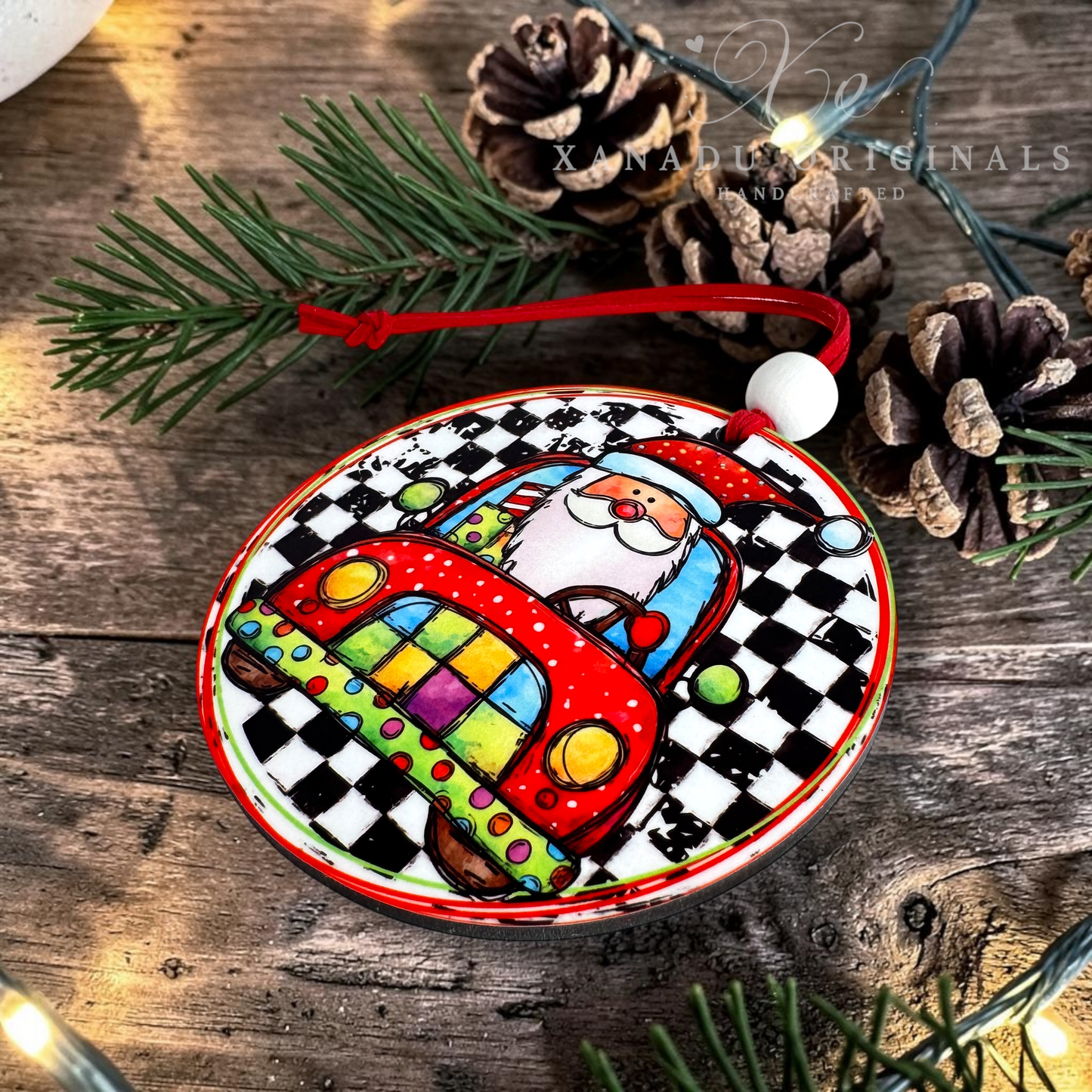 A round ceramic Christmas ornament featuring a colorful Santa driving a red checkered car, displayed on a rustic wooden surface with pine branches and pinecones.