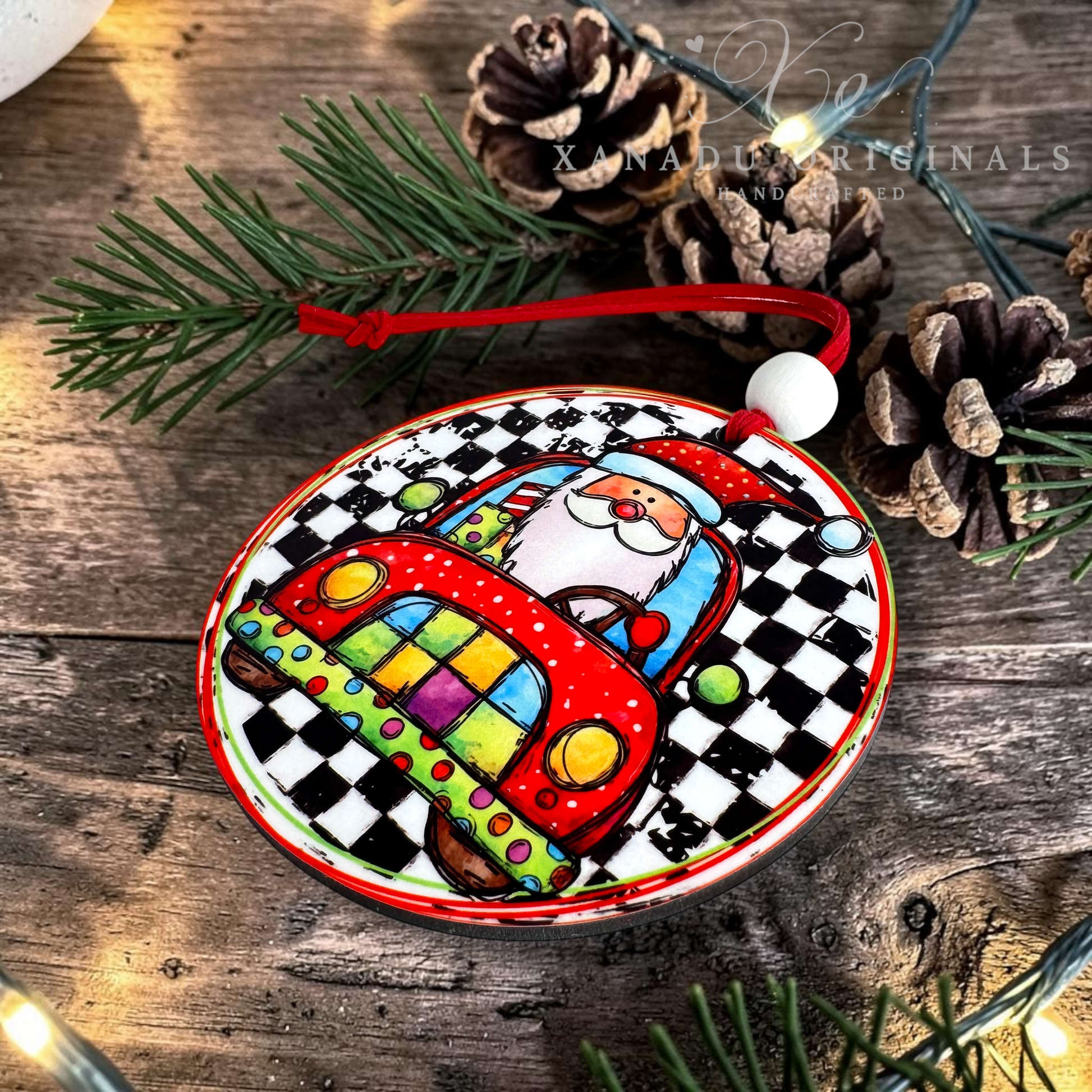 A round ceramic Christmas ornament featuring a colorful Santa driving a red checkered car, displayed on a rustic wooden surface with pine branches and pinecones.