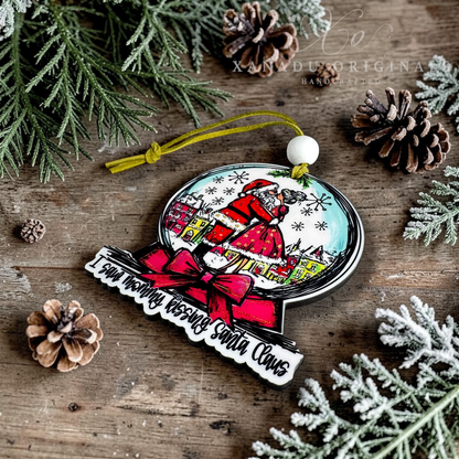A Christmas ornament featuring an illustration of Santa Claus in a snowy village scene, with a red bow and the text 'I saw mommy kissing Santa Claus' on a rustic wooden background with pine branches and pinecones.