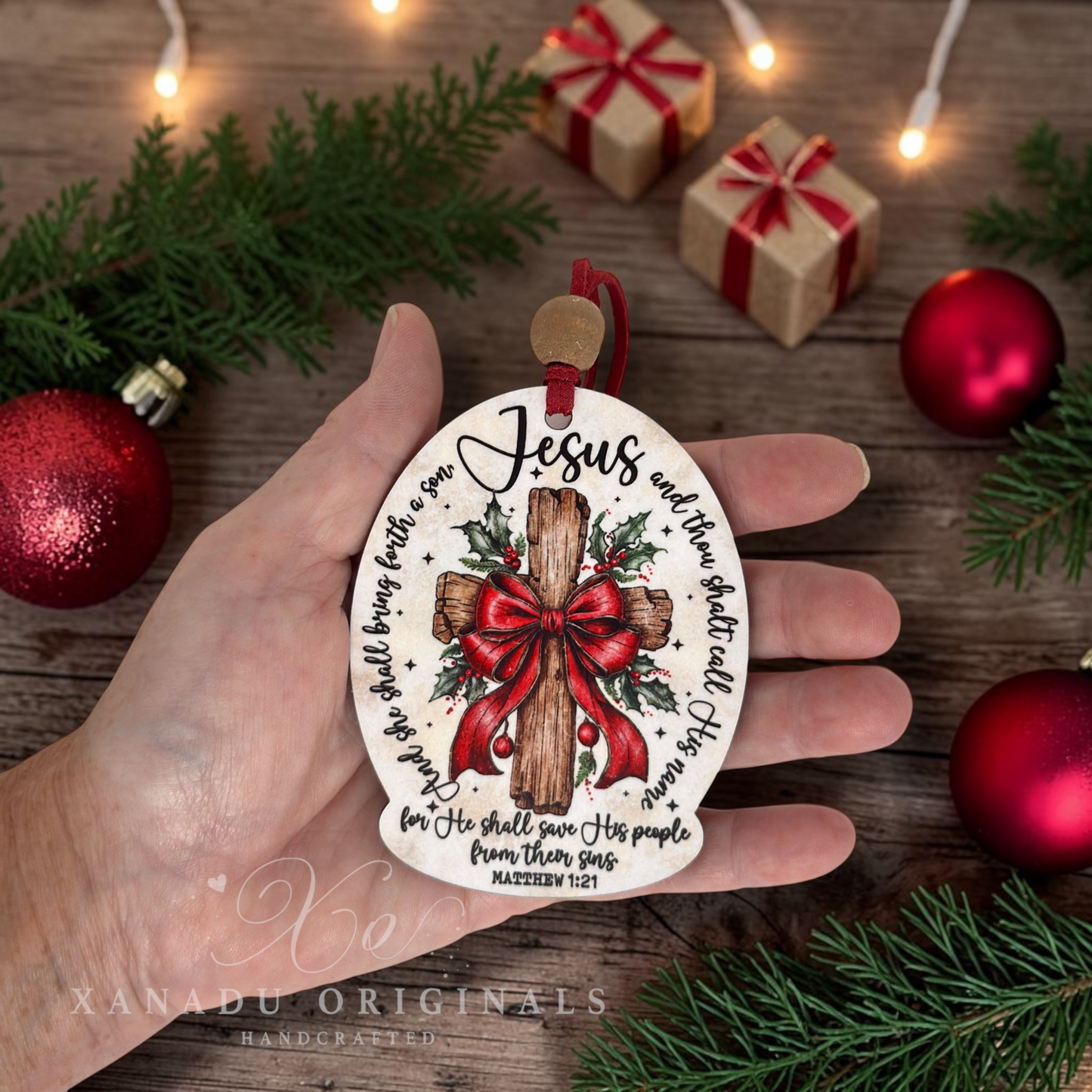 A hand holds a round Christmas ornament featuring a wooden cross with a red bow, holly, and the text 'Jesus and the world apart all His love.