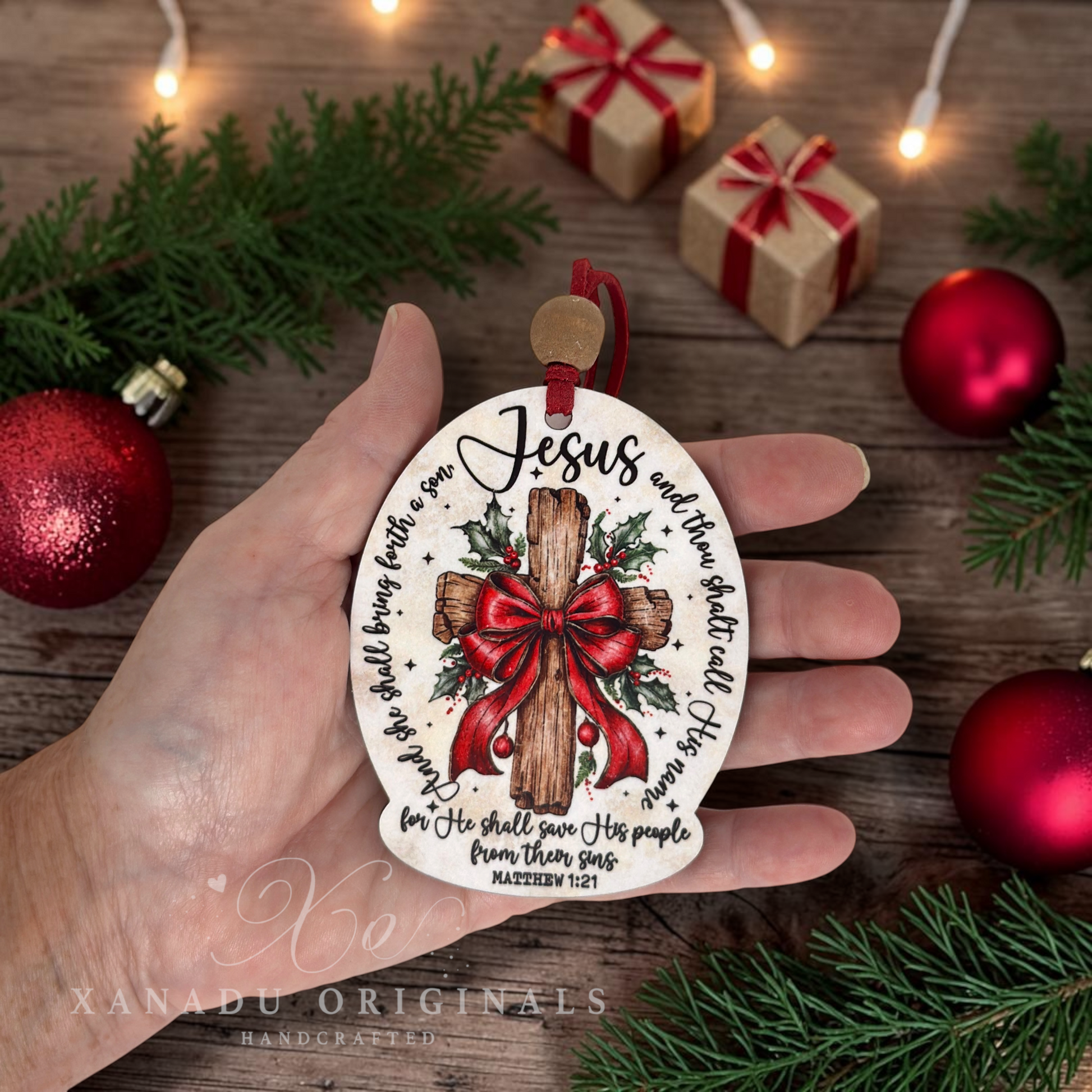 A hand holds a round Christmas ornament featuring a wooden cross with a red bow, holly, and the text 'Jesus and the world apart all His love.