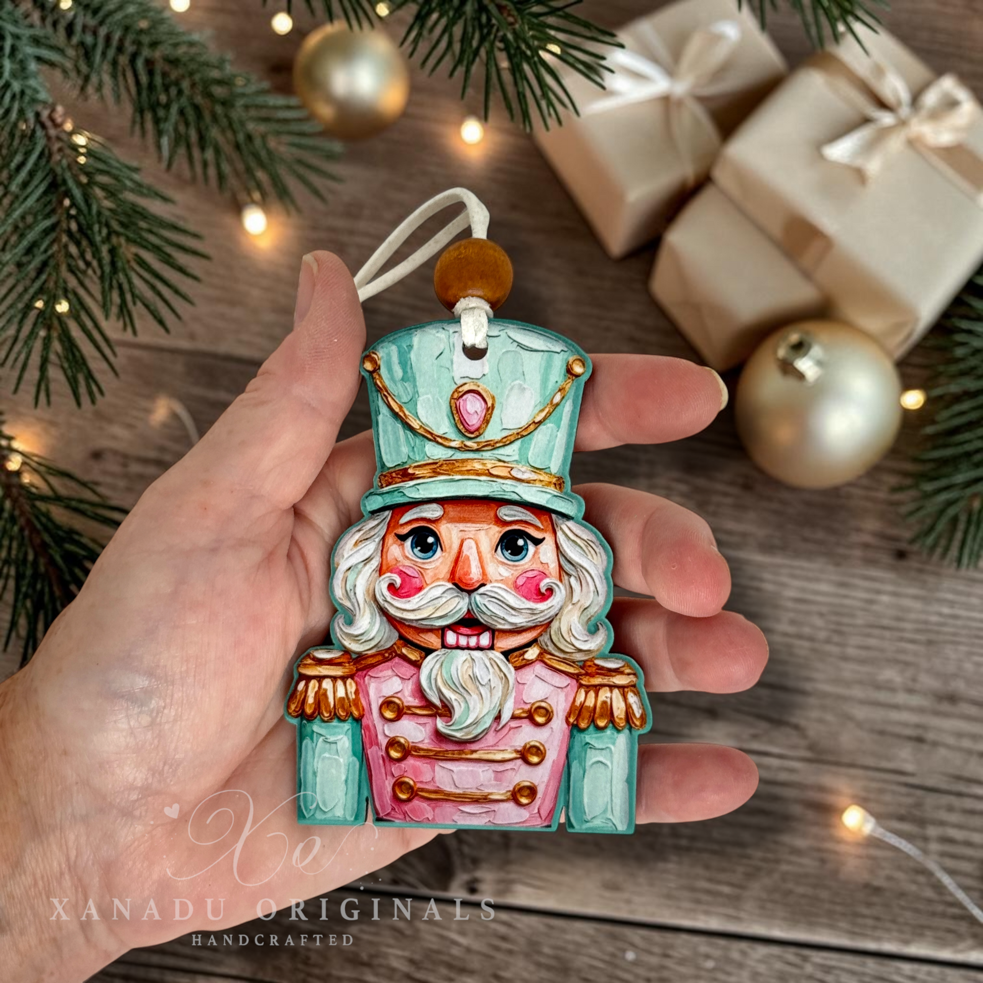 A hand holds a hand-painted wooden Christmas nutcracker ornament. The ornament features a turquoise hat and coat with gold trim, a pink jacket, and a white beard.