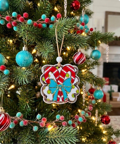 A close-up of a decorated Christmas tree with a central candy cane ornament featuring red and white striped candy canes and a bright blue bow, surrounded by teal and red baubles and warm string lights.