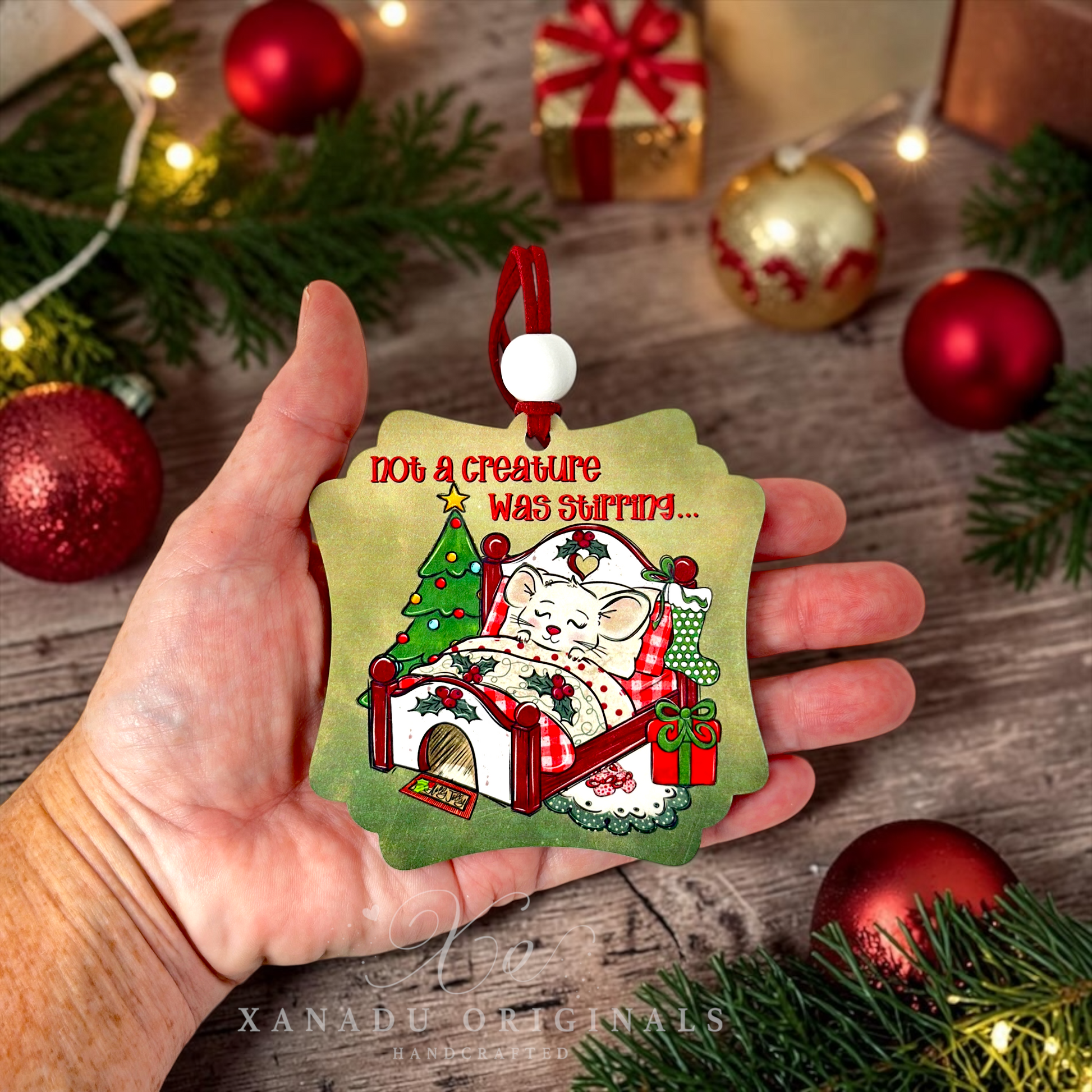 A hand holds a Christmas ornament shaped like a mouse in bed under a tree, with the text 'Not a creature was stirring.
