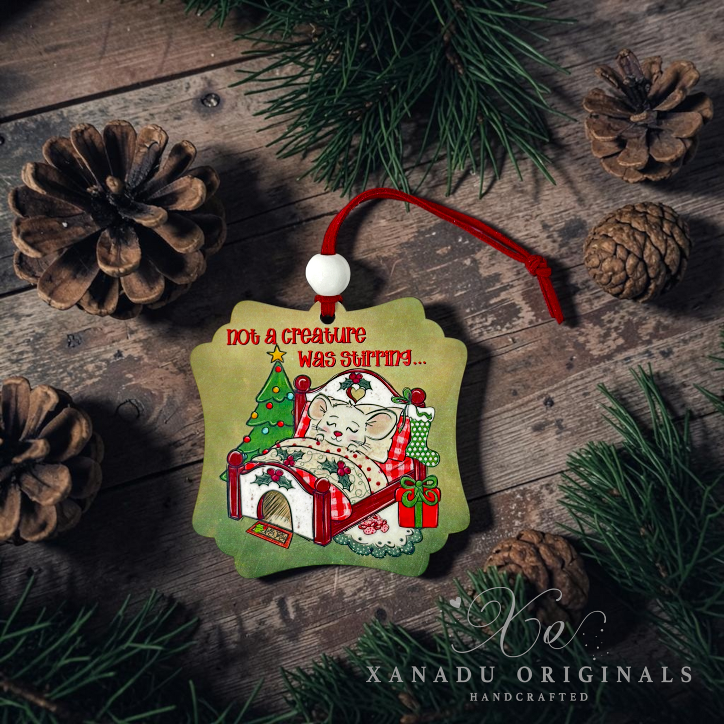 A handcrafted Christmas ornament shaped like a green house, featuring a white cat sleeping inside with a red holiday theme and the text 'Not a creature was snuff'd.