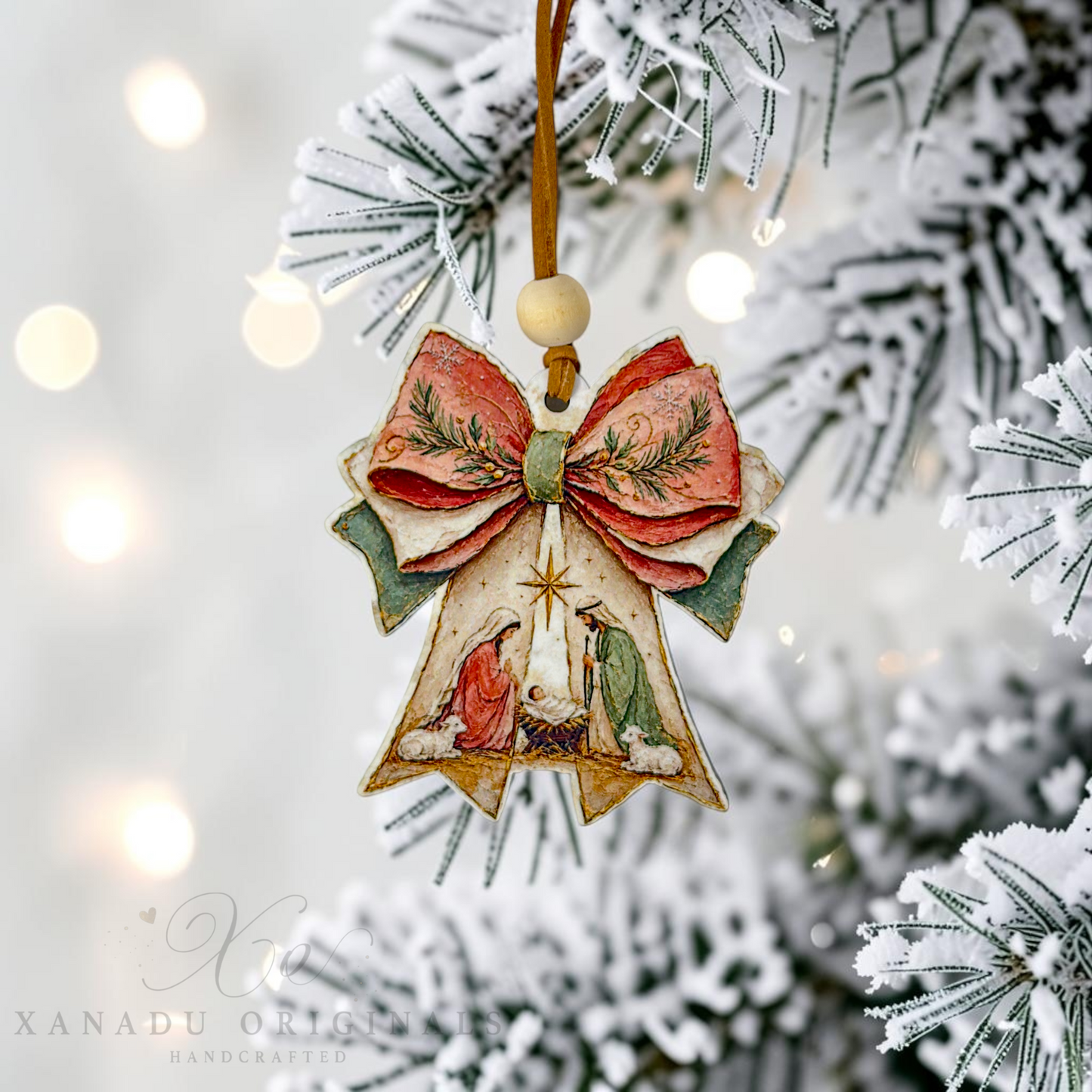 A handcrafted wooden Christmas nativity ornament shaped like a bow and arrow, hanging from a flocked Christmas tree branch with warm bokeh lights in the background. The ornament features a red bow with green pine details, a wooden bead, and a carved nativity scene with Mary, Joseph, and baby Jesus.