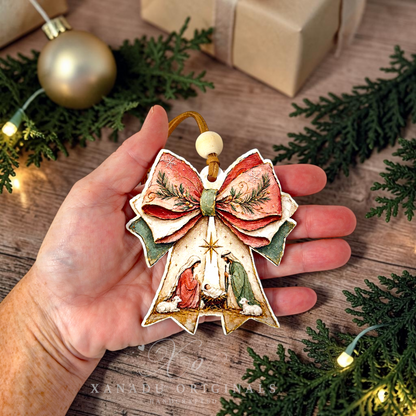 A hand holds a decorative Christmas angel ornament shaped like a bell with a large bow. The ornament has a cream base with red, green, and gold painted details, including a star and figures in robes.