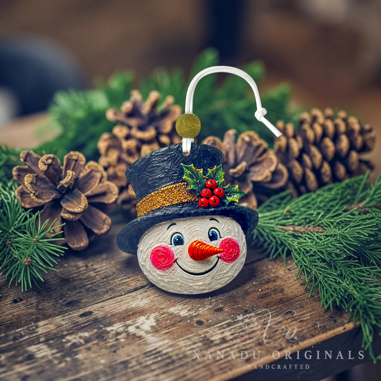 A handcrafted wooden snowman ornament with a black hat, red berries, and a white hanging loop, styled on a rustic wooden surface with pine branches and pinecones in the background.