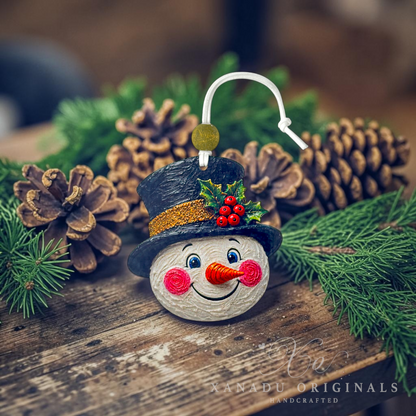 A handcrafted wooden snowman ornament with a black hat, red berries, and a white hanging loop, styled on a rustic wooden surface with pine branches and pinecones in the background.