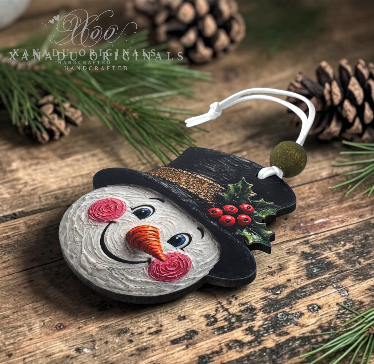 A handcrafted wooden snowman ornament with a black hat, pink cheeks, an orange carrot nose, and a green holly accent, resting on a rustic wooden surface with pine needles and pinecones.