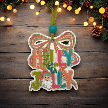 A handcrafted wooden Christmas ornament shaped like a bow with the words 'Holly & Jolly' in colorful lettering, hanging on a rustic dark wood background with warm string lights and pine branches.