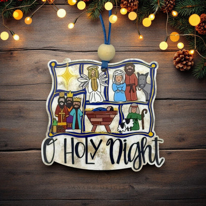 A decorative wooden Christmas ornament shaped like a scroll with a nativity scene and the words “O Holy Night” in script, hanging against a rustic wooden background with string lights and pine branches.