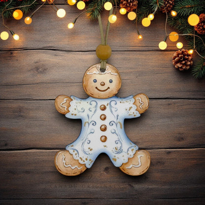 A hand-painted gingerbread man Christmas ornament hangs on a rustic dark wood background, decorated with light blue icing, gold buttons, and white icing details. The scene is decorated with pine branches and warm glowing fairy lights.