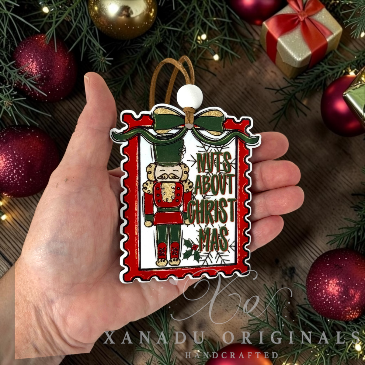Funny whimsical nutcracker Christmas ornament measuring 3.21 by 3.75 inches held in a hand next to holiday tree decorations.
