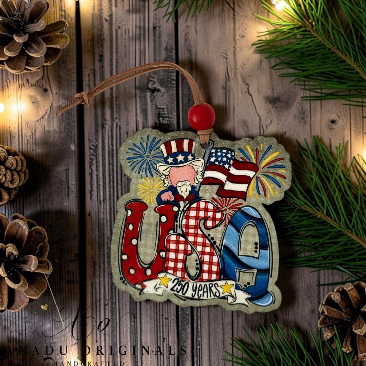 A decorative wooden USA 250 Years hanging ornament with Uncle Sam, fireworks, and an American flag design, shown on a rustic wood background with pine branches and warm string lights.