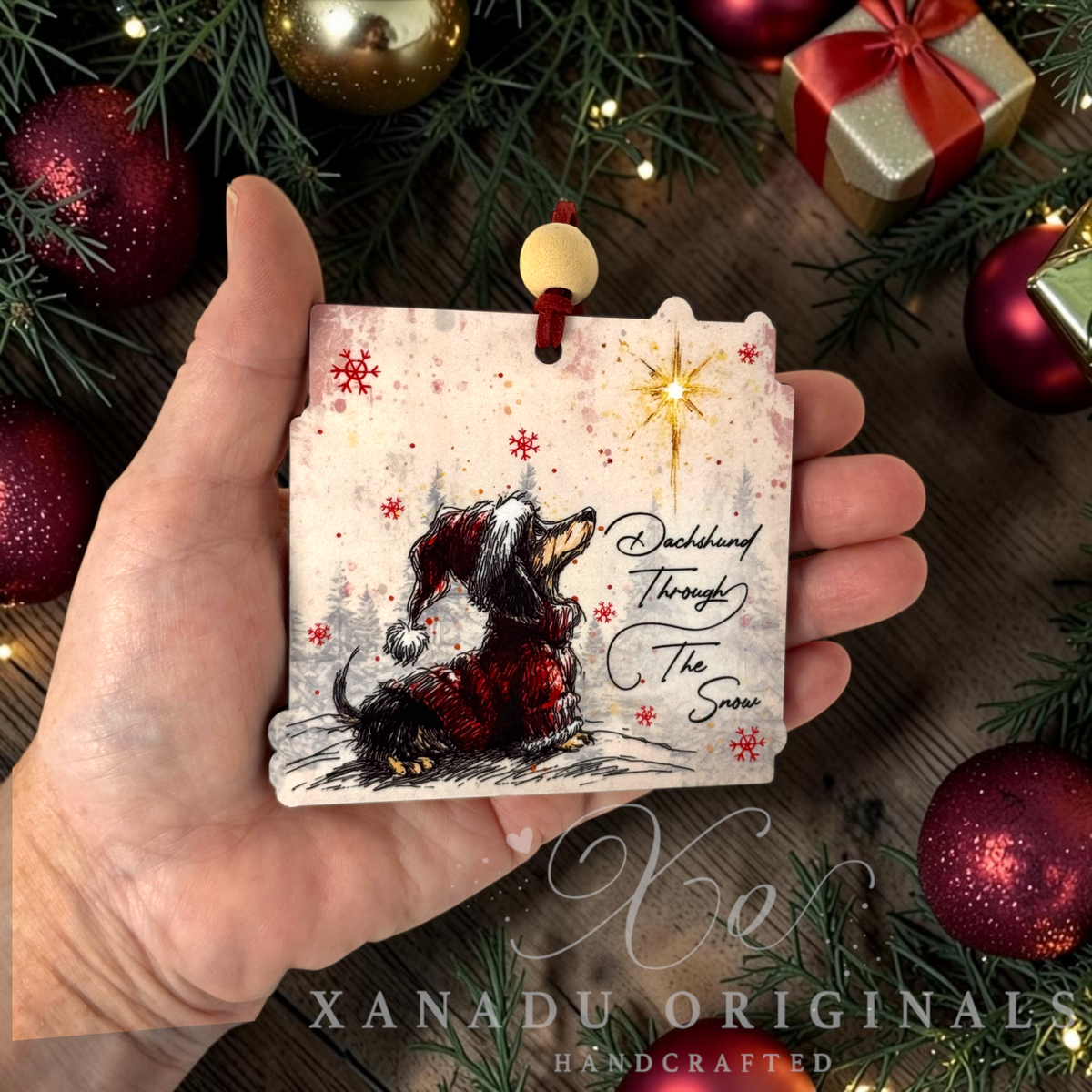 Whimsical pet lover Dachshund Christmas ornament measuring 3.5 by 3.38 inches held in a hand next to holiday tree decorations.