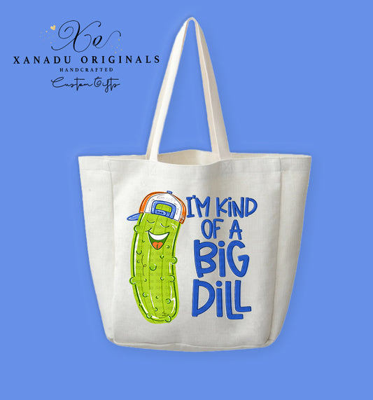 A cream-colored polyester linen tote bag featuring a bright cartoon illustration of a smiling pickle character wearing a backwards baseball cap next to the blue text "I'M KIND OF A BIG DILL".