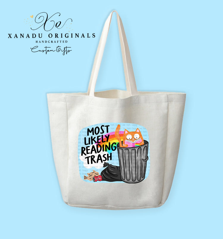 A cream-colored polyester linen tote bag featuring a cartoon illustration of a wide-eyed orange cat with rosy cheeks sitting inside a grey metal trash can, reading a book with a rainbow cover. To the left, bold black and teal text reads "MOST LIKELY READING TRASH" next to a black garbage bag.