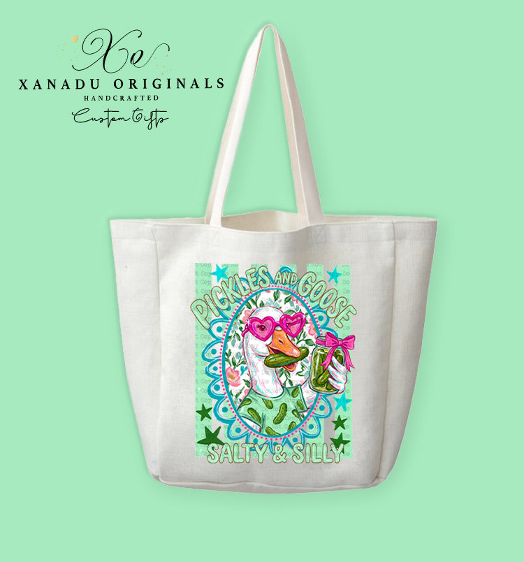 A cream-colored polyester linen tote bag featuring a bright mint and pink illustration of a goose wearing heart glasses and eating a pickle next to the text "PICKLES AND GOOSE SALTY & SILLY".