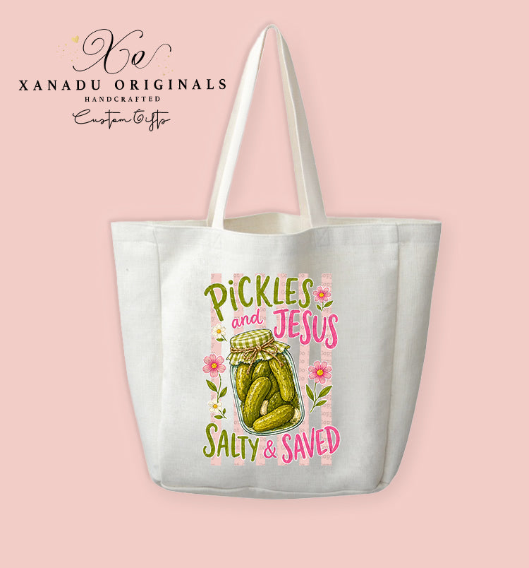 A cream-colored polyester linen tote bag featuring a colorful illustration of a pickle jar surrounded by pink stripes and daisies with the text "PICKLES AND JESUS SALTY & SAVED".