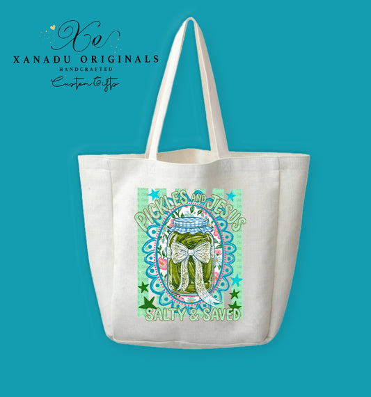 A cream-colored polyester linen tote bag featuring a colorful illustration of a pickle jar tied with a lace bow, surrounded by teal patterns, flowers, and the text "PICKLES AND JESUS SALTY & SAVED".