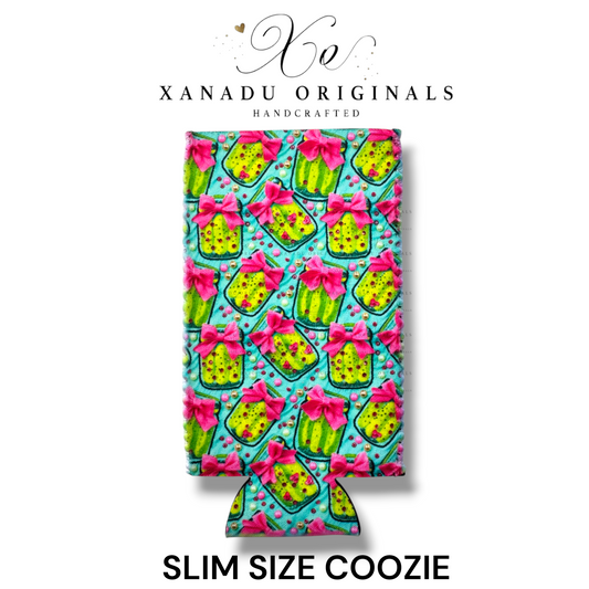 "Xanadu Originals handcrafted slim size neoprene can coozie featuring a vibrant repeating pattern of neon green pickle jars with bright pink bows against a turquoise background."