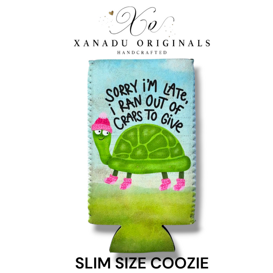 "Xanadu Originals handcrafted slim size neoprene can coozie featuring a slow-moving green turtle wearing a pink winter hat and socks with the sarcastic text 'Sorry I'm late, I ran out of craps to give' on a soft green and blue background."