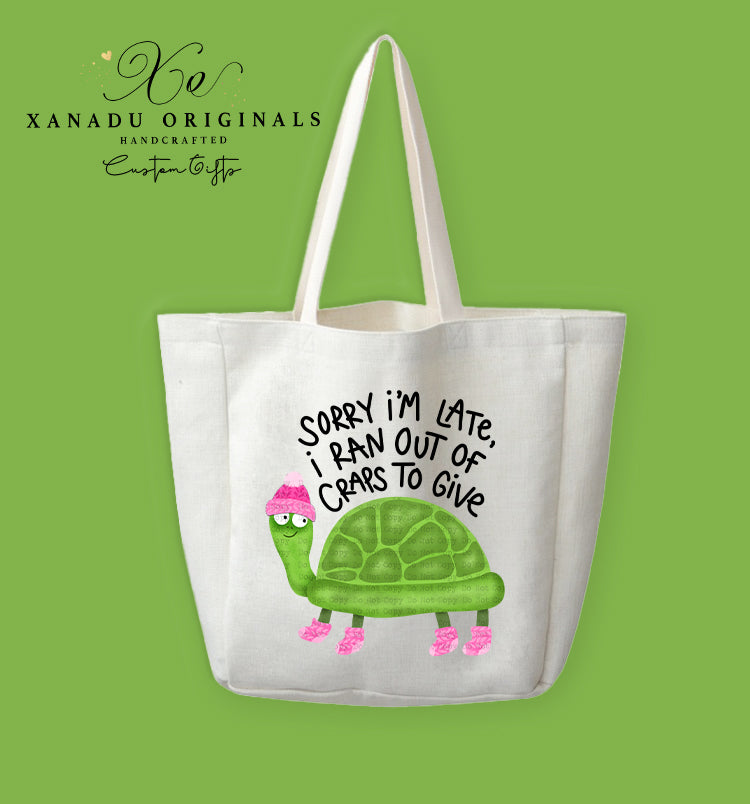 A cream-colored polyester linen tote bag featuring a cartoon illustration of a smiling green turtle wearing a pink winter hat and four pink leg warmers. Bold black text arched above the graphic reads "SORRY I'M LATE, i RAN OUT OF CRAPS To Give."