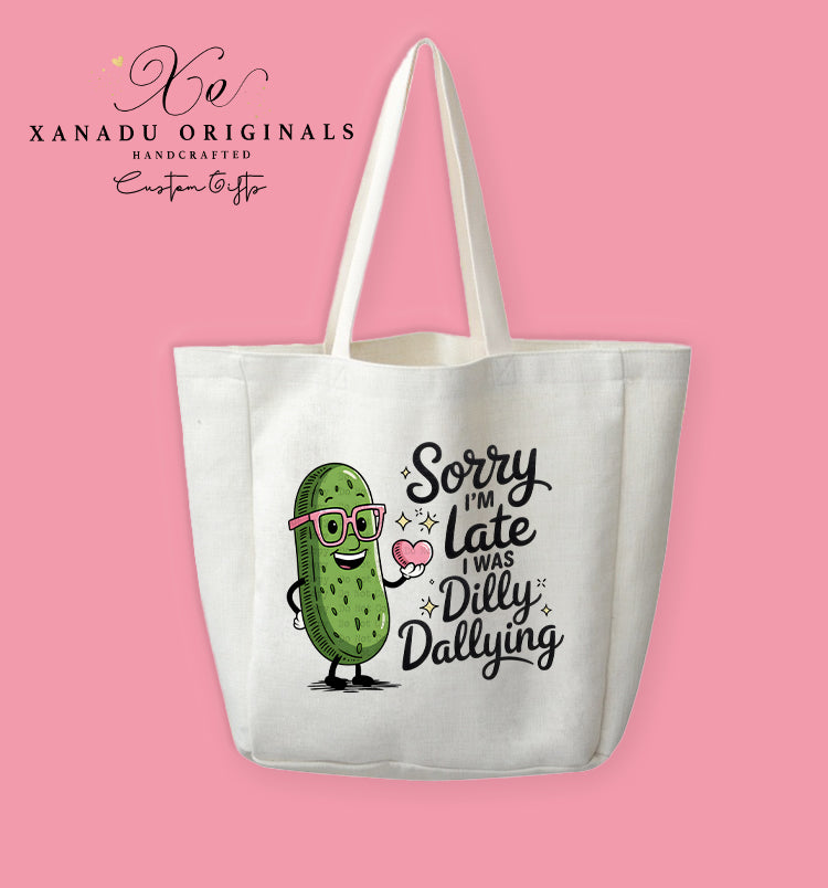 A cream-colored polyester linen tote bag featuring a cute cartoon illustration of a smiling pickle wearing pink glasses and holding a heart next to the text "Sorry I'm late, I was Dilly Dallying".