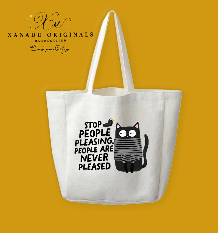 A cream-colored polyester linen tote bag featuring a cartoon illustration of a wide-eyed black cat wearing a grey and black striped sweater with a small black bird sitting on its head. To the left, bold black text reads "STOP PEOPLE PLEASING. PEOPLE ARE NEVER PLEASED."
