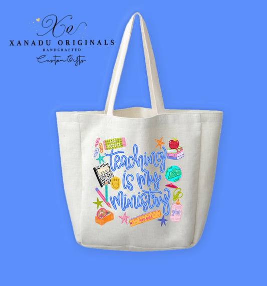 A cream-colored polyester linen tote bag featuring a collage of colorful classroom doodles including a composition notebook, a globe, an apple on books, a ruler, and glue surrounding stylized blue script text that reads "Teaching is my Ministry."