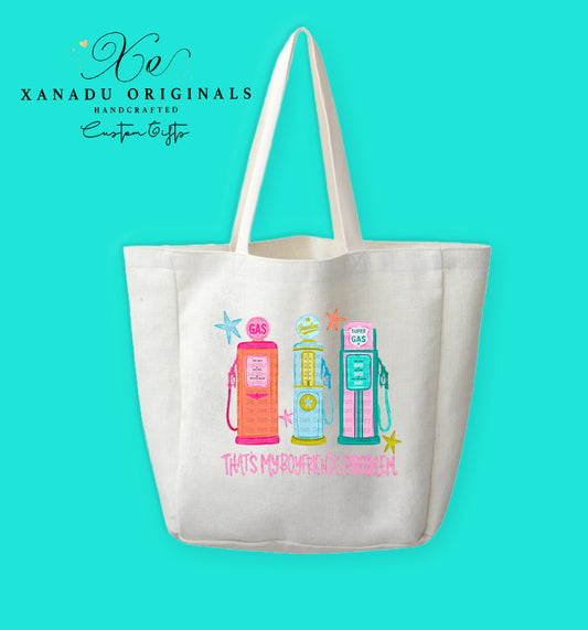 A cream-colored polyester linen tote bag featuring a retro mid-century modern graphic of three vintage gas pumps in pink, yellow, and teal with starburst details. Bright pink stylized text underneath reads "THAT'S MY BOYFRIEND'S PROBLEM."