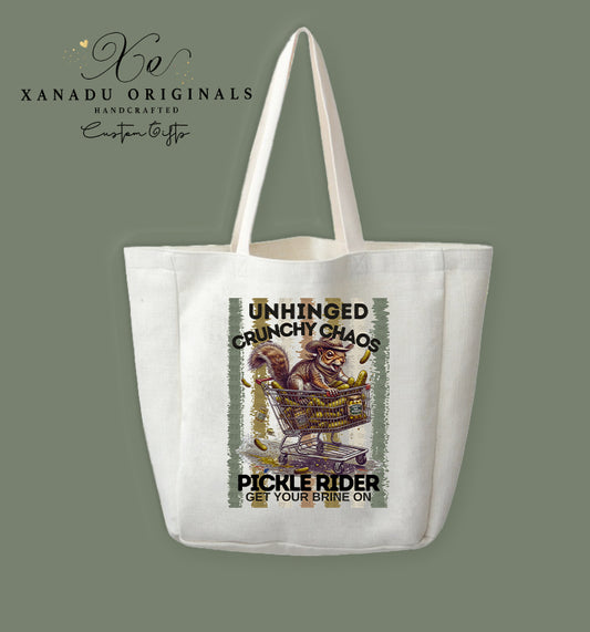 A cream-colored polyester linen tote bag featuring a distressed vintage-style illustration of a squirrel in a cowboy hat riding in a shopping cart full of pickles.