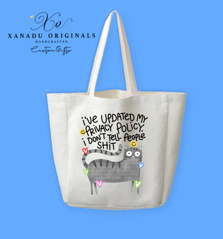 A cream-colored polyester linen tote bag featuring a cartoon illustration of a wide-eyed grey striped tabby cat surrounded by small colorful neon heart outlines. Bold black text above the cat reads "I've UPDATED My PRIVACY POLICY. i DON'T Tell PeOPle SHIT" with tiny yellow smiley faces.