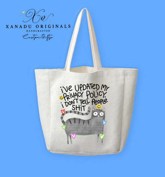 A cream-colored polyester linen tote bag featuring a cartoon illustration of a wide-eyed grey striped tabby cat surrounded by small colorful neon heart outlines. Bold black text above the cat reads "I've UPDATED My PRIVACY POLICY. i DON'T Tell PeOPle SHIT" with tiny yellow smiley faces.