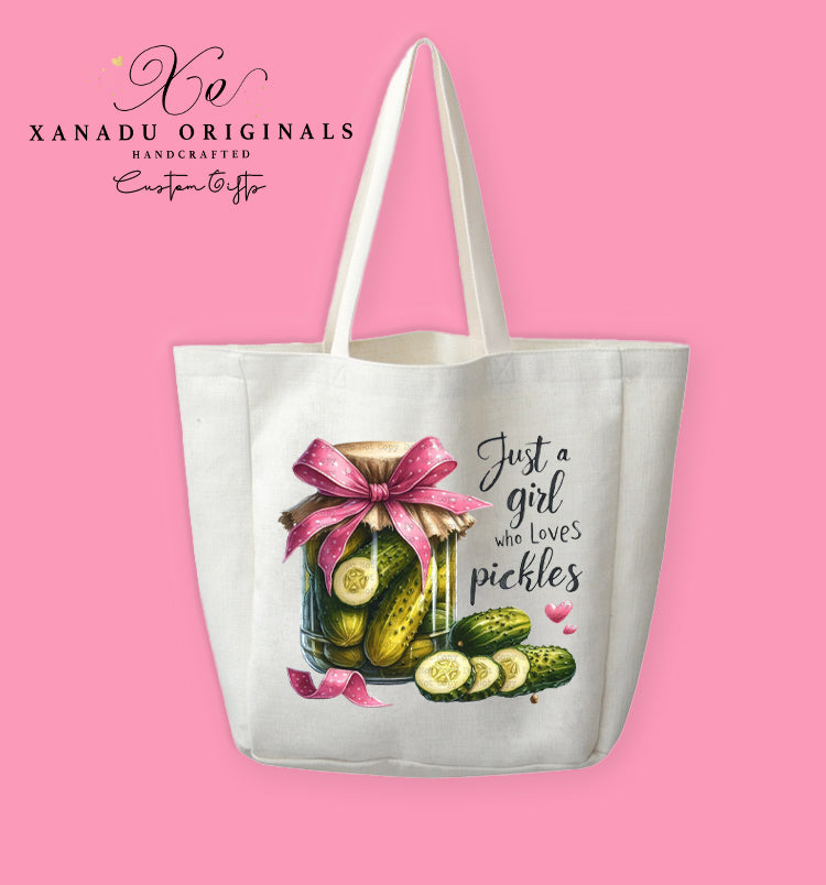 A cream-colored polyester linen tote bag featuring a watercolor illustration of a pickle jar tied with a pink polka-dot bow next to the script text "Just a girl who loves pickles".