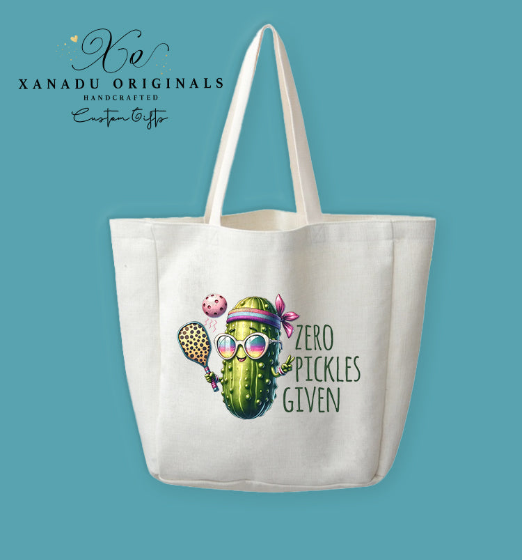 A cream-colored polyester linen tote bag featuring a colorful illustration of a sporty pickle wearing sunglasses and a headband while playing pickleball next to the text "ZERO PICKLES GIVEN".