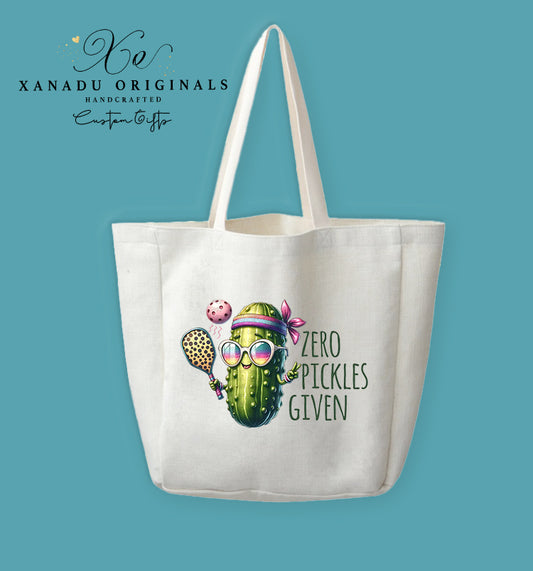 A cream-colored polyester linen tote bag featuring a colorful illustration of a sporty pickle wearing sunglasses and a headband while playing pickleball next to the text "ZERO PICKLES GIVEN".